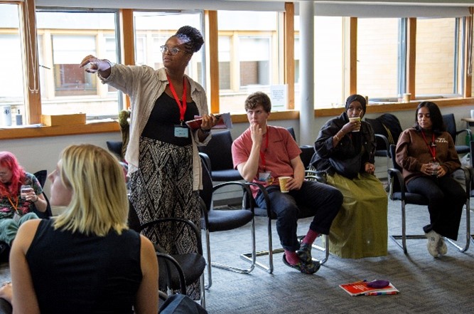 A person standing in a room with people sitting in chairs