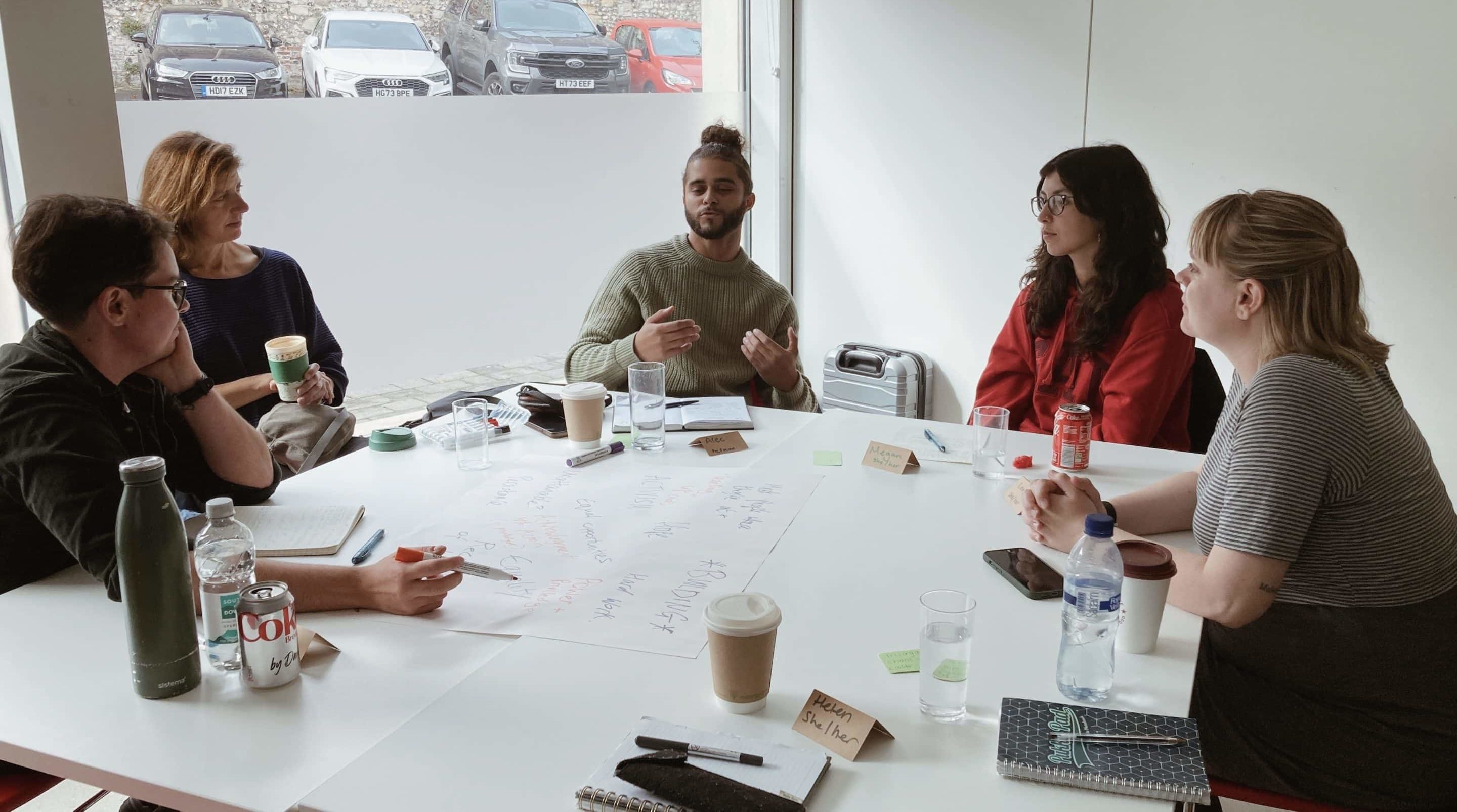 Group of people sitting around a table with pens and paper.