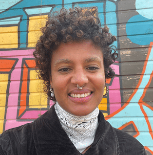 Person with curly hair taking a selfie infront of a colourful wall